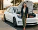 Editorial magazine photography of a stylish Asian woman standing beside a white Tesla, hand resting lightly on the open