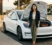 Editorial magazine photography of a stylish Asian woman standing beside a white Tesla, hand resting lightly on the open